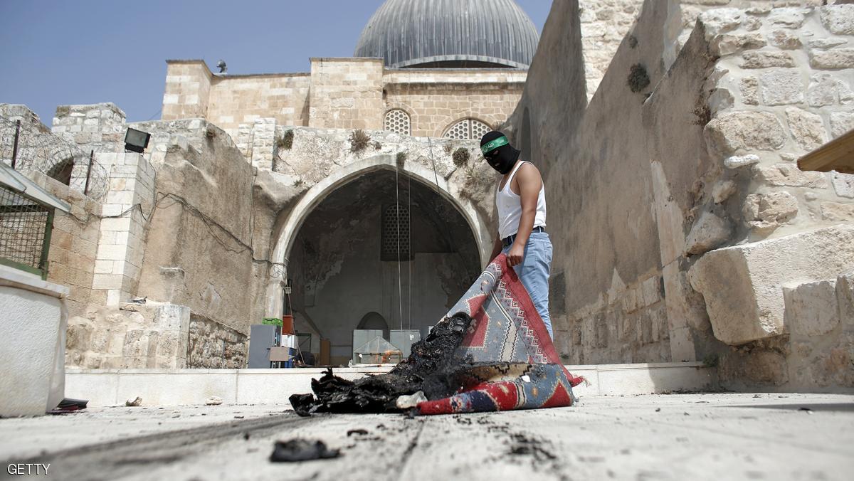 A masked Palestinian wearing a Hamas headband takes a burnt carpet out of Al-Aqsa mosque in Jerusalem's Old City during clashes at the compound on September 13, 2015, just hours before the start of the Jewish New Year. The disturbances came with tensions running high after Israeli Defence Minister Moshe Yaalon last week outlawed the Murabitat (for females) and Murabitun groups which are made up of east Jerusalem Palestinians and Israeli Arabs and who confront Jewish visitors to the volatile Al-Aqsa mosque complex, considered Islam's third holiest shrine. AFP PHOTO / AHMAD GHARABLI (Photo credit should read AHMAD GHARABLI/AFP/Getty Images)